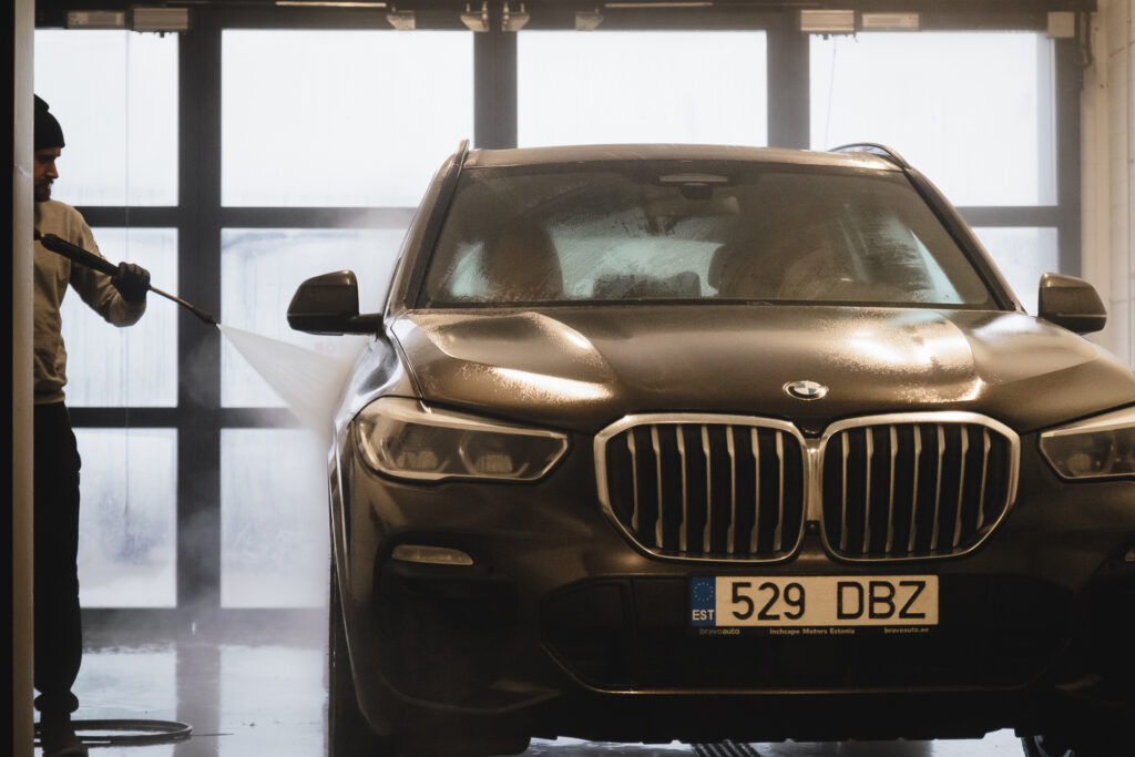 BMW X5 detailne käsipesu – töötaja loputab survepesuriga sõiduki esitiiba ja külge professionaalses pesuboksis.