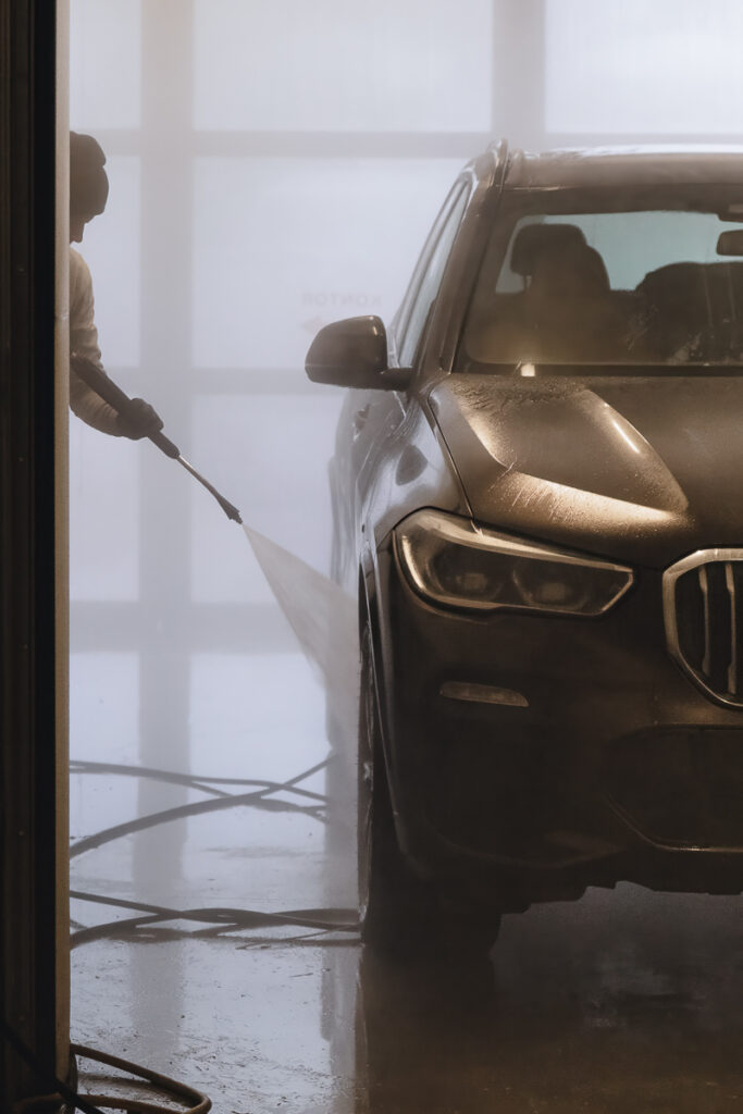 BMW X5 detailne käsipesu – töötaja loputab survepesuriga sõiduki esitiiba ja külge professionaalses pesuboksis.