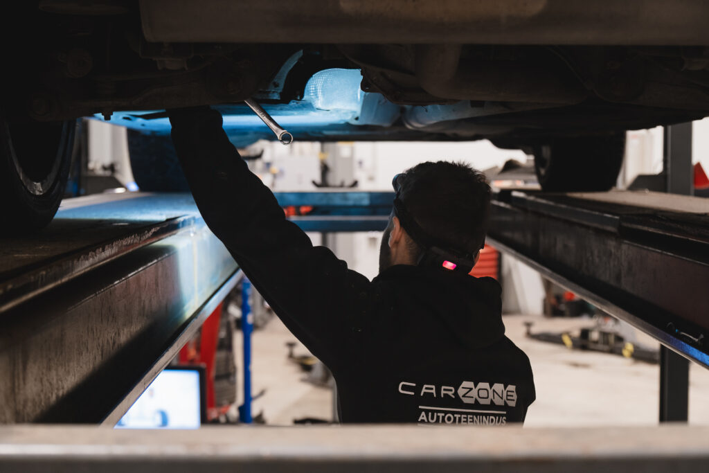 Carzone autoteeninduse mehaanik töötab tõstukil oleva sõiduki all, teostades hooldus- või remonditöid töökojas.
